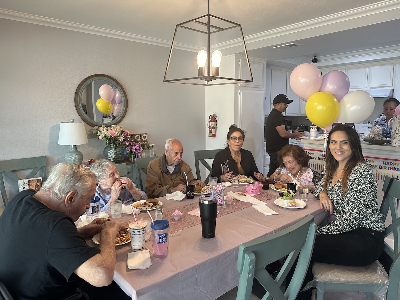 A group of people celebrating a birthday at a dining table with balloons and decorations.