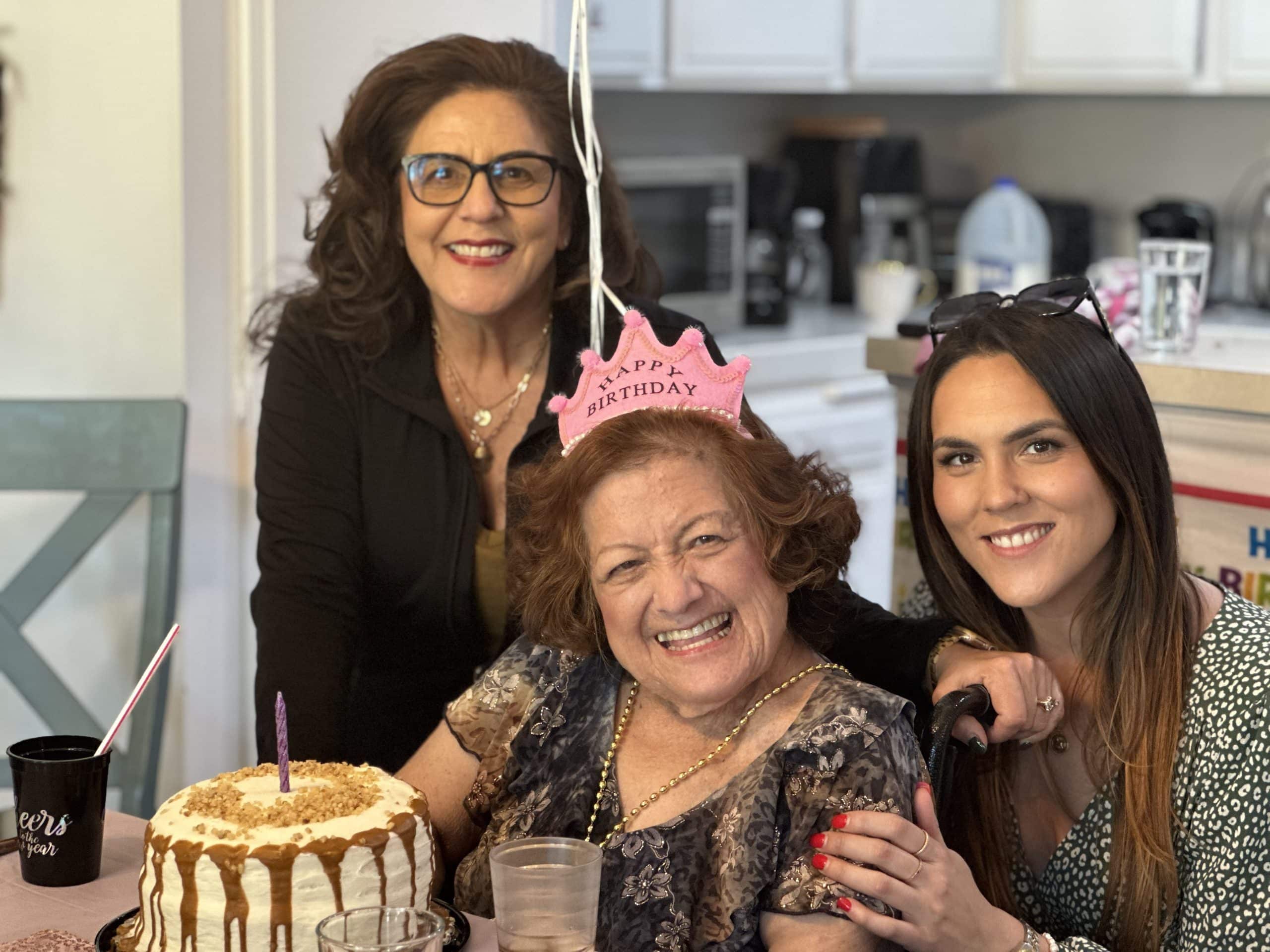 Three women celebrating a birthday with a cake and pink birthday crown.