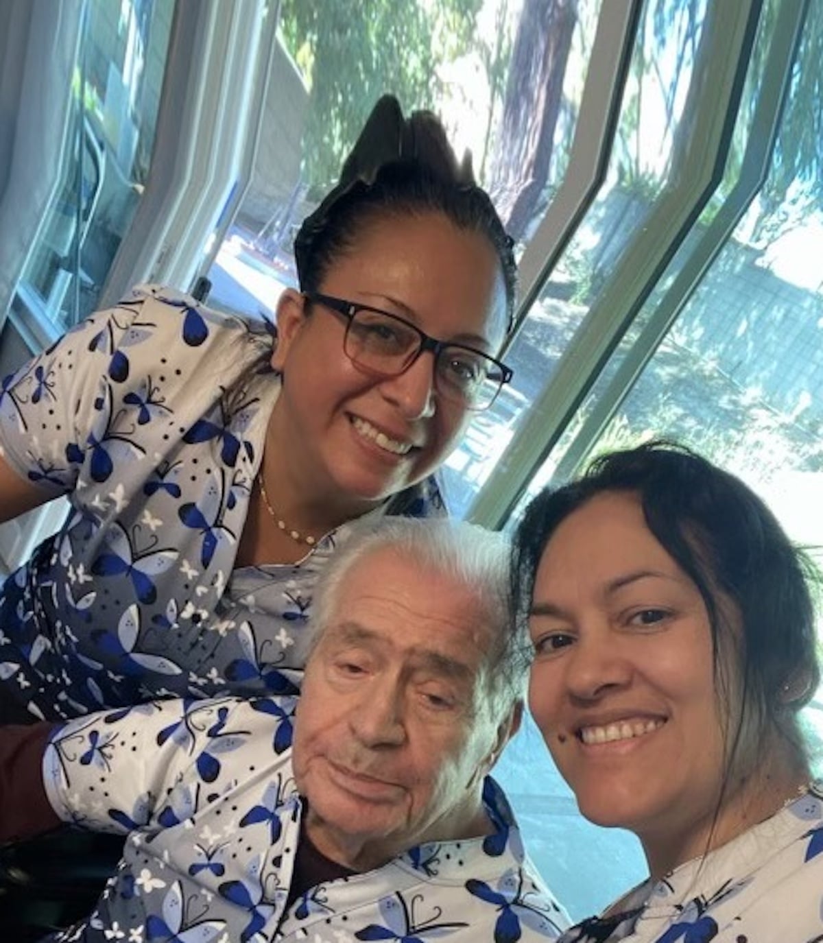 Two women and an older man in matching butterfly-themed shirts smiling indoors.