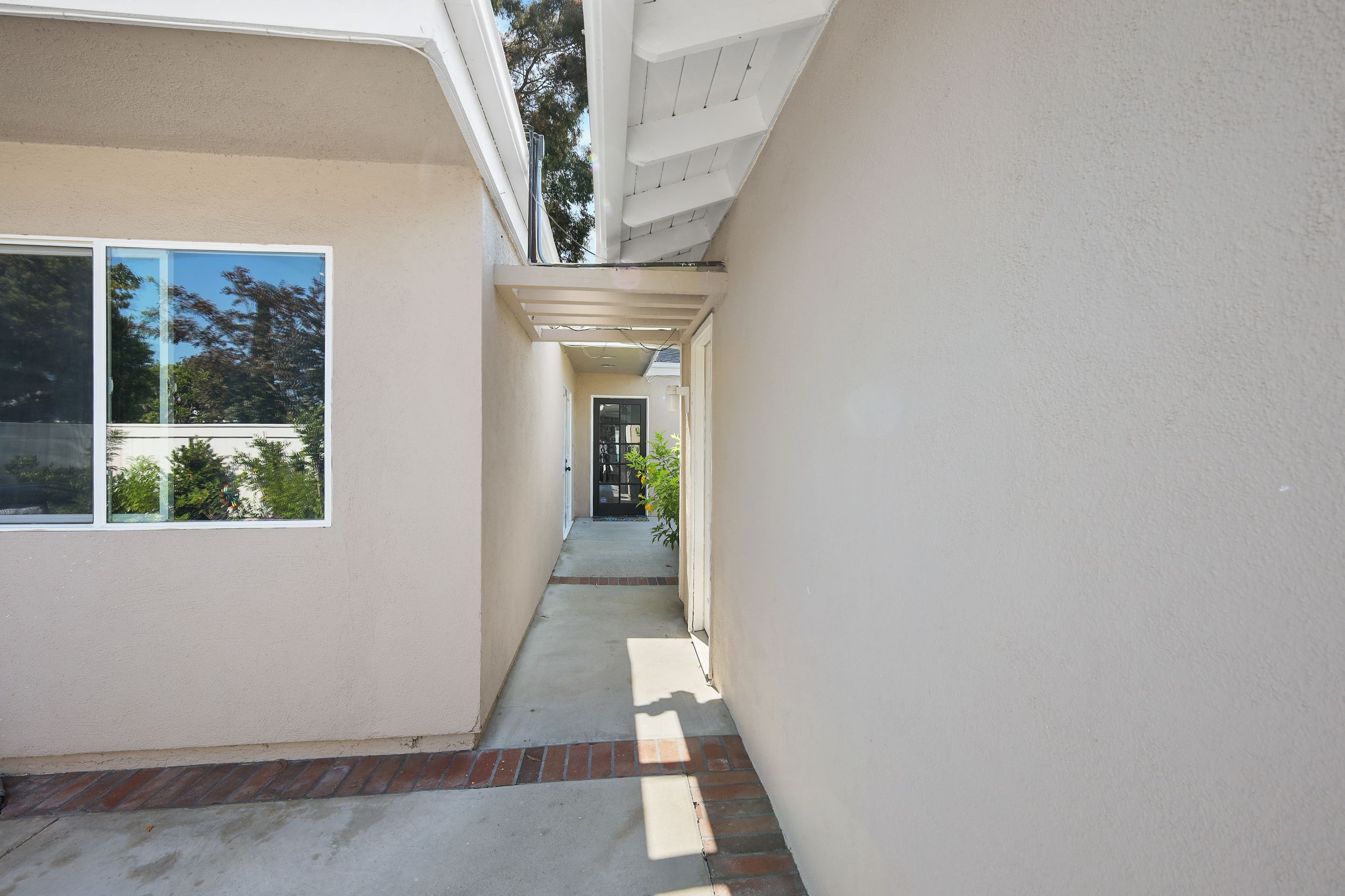 Narrow outdoor walkway between two tall beige walls with a window on the left side.