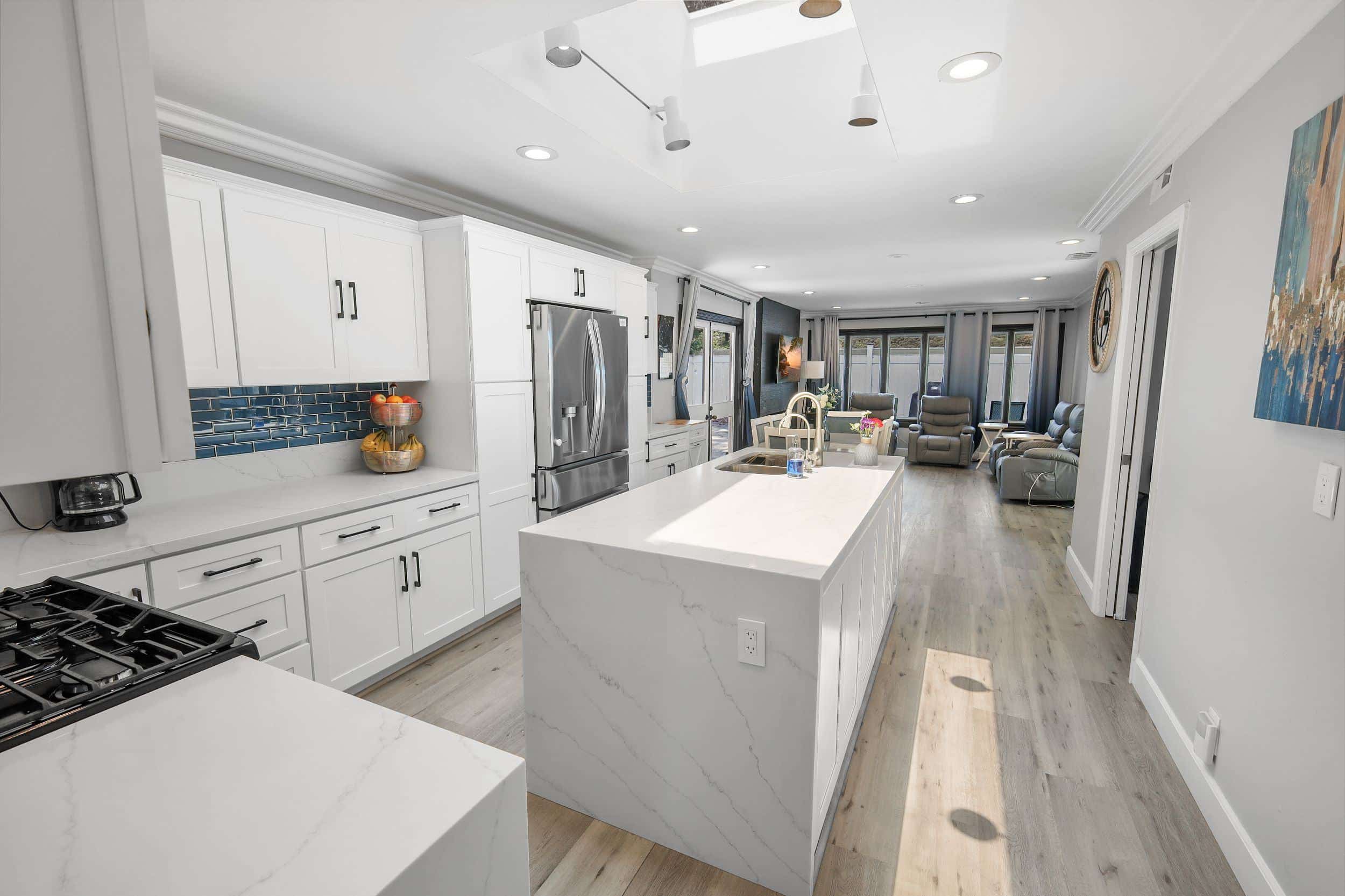 Modern kitchen with white cabinets, marble countertops, stainless steel appliances, and open living area in bright home.