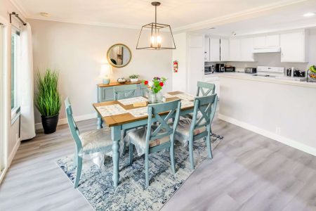 Cozy dining room with teal furniture, vase of flowers, and round mirror on the wall.