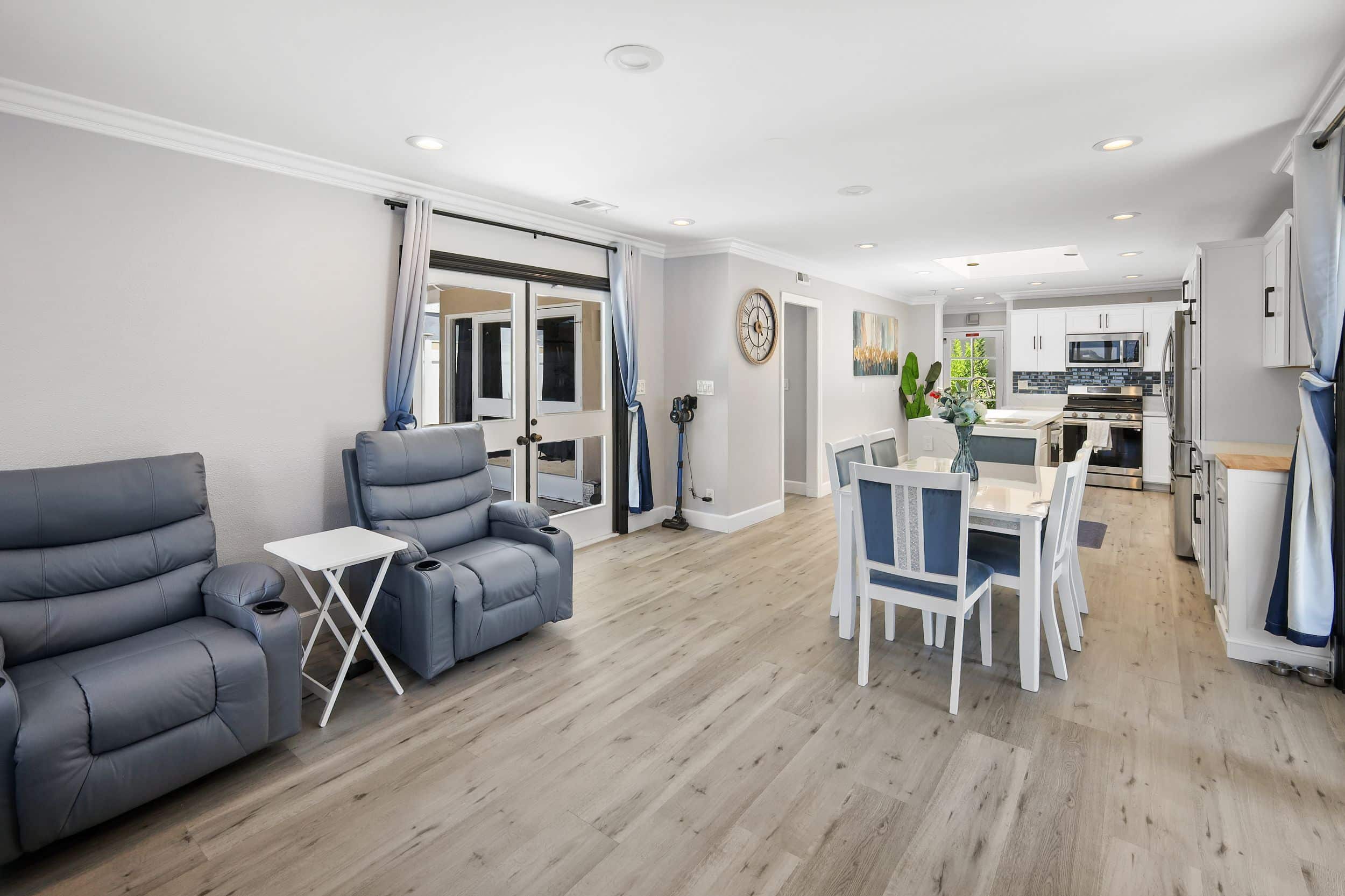 Modern open-plan living room and kitchen with gray armchairs and white dining set.