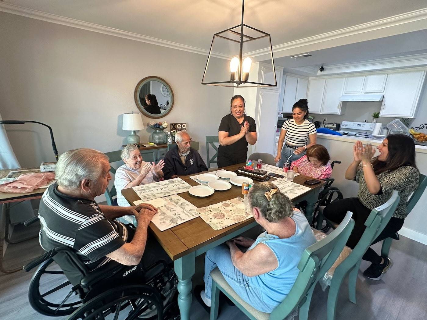 People gathered around a table in a living room, clapping and socializing.