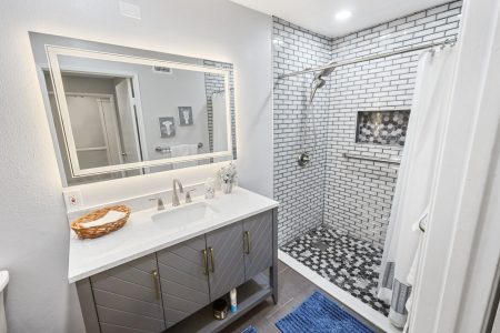 Modern bathroom with a gray vanity, large mirror, and walk-in shower with white subway tiles.
