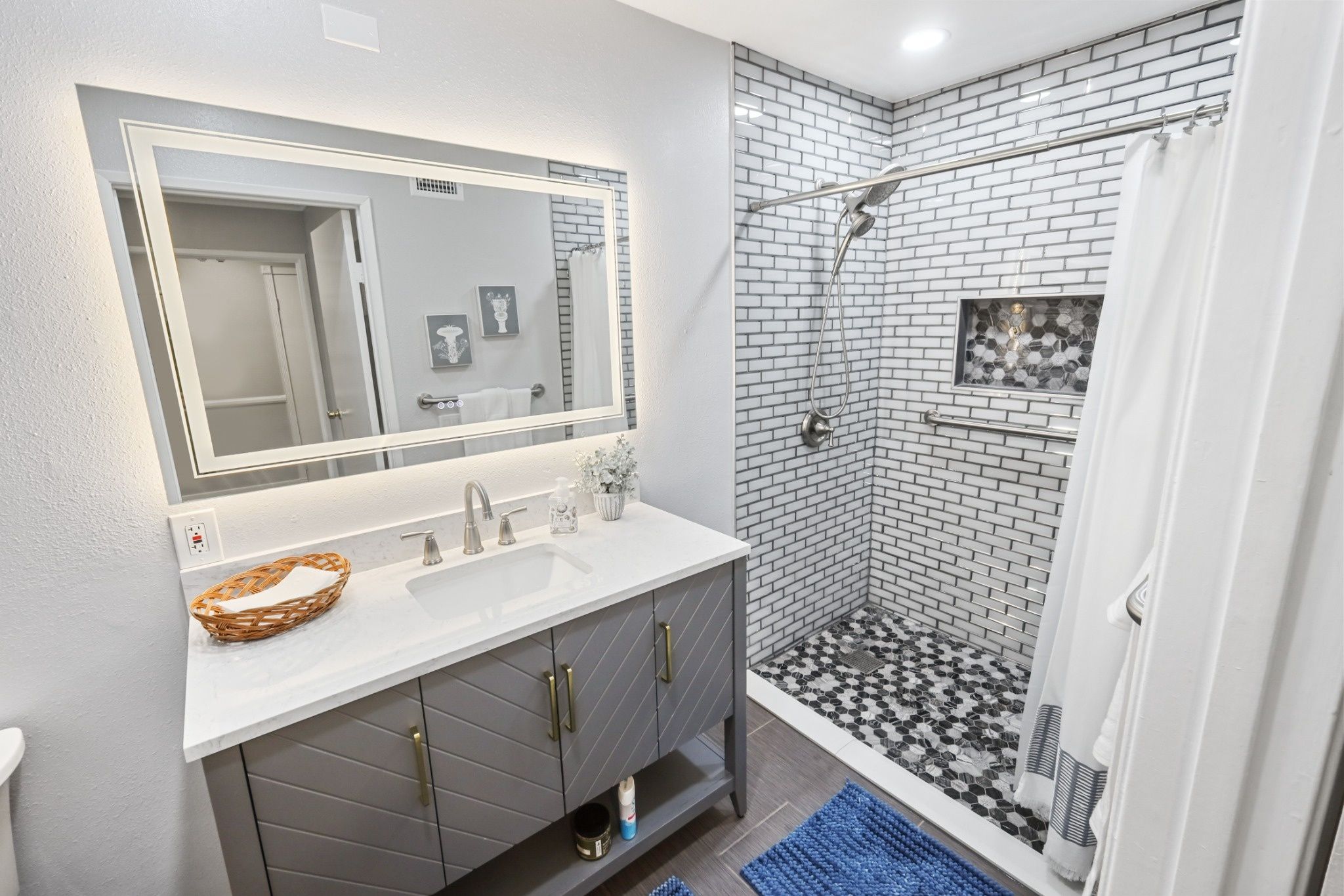 Modern bathroom with a gray vanity, large mirror, and walk-in shower with white subway tiles.