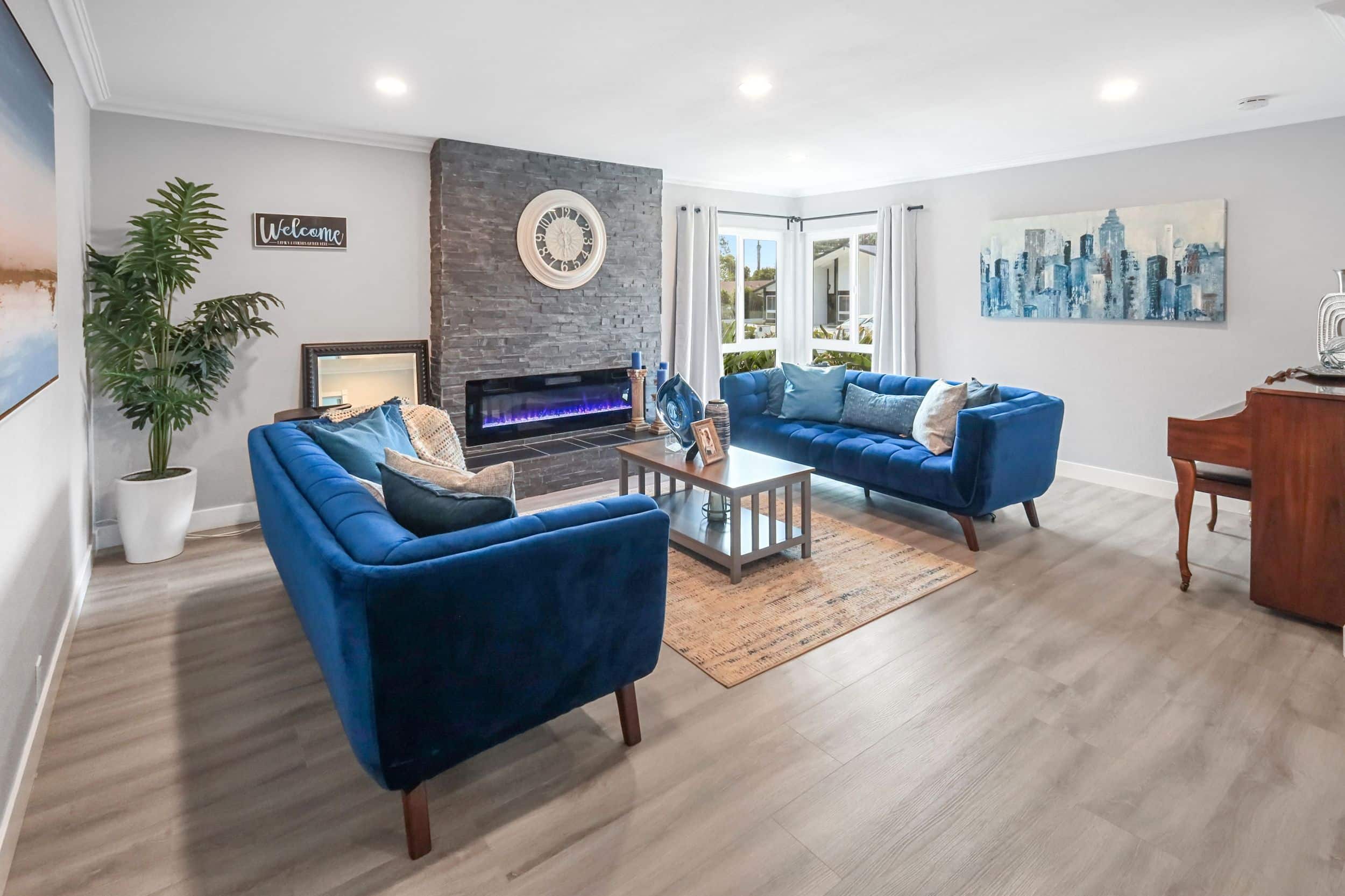 Modern living room with blue sofas, fireplace, and large window.