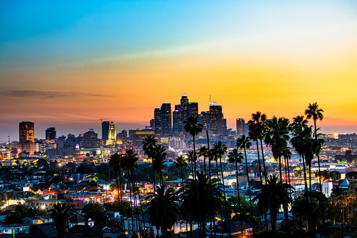 Los Angeles skyline at sunset with silhouetted palm trees in the foreground.