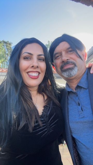 A woman and a man smiling in outdoor sunlight with trees in the background.