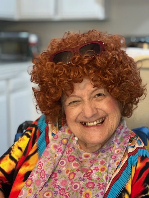 A smiling woman with curly red hair and sunglasses indoors.