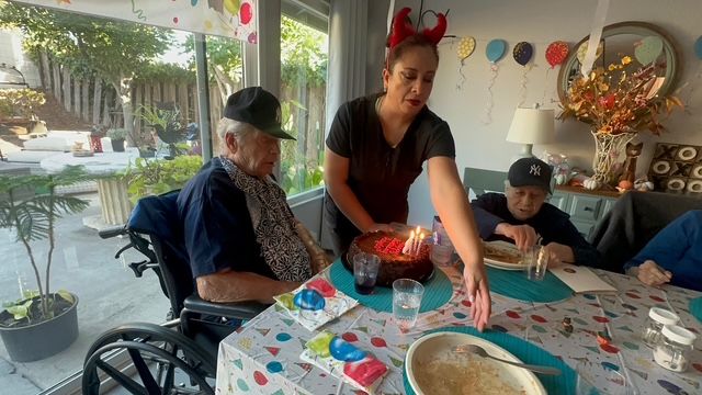 A woman with a cake celebrating a birthday with elderly people at a decorated table.