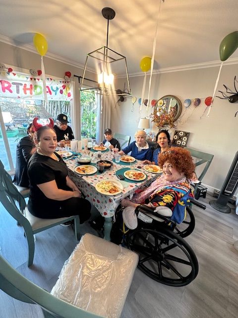 A family gathered around a table with a birthday banner and balloons in the background.